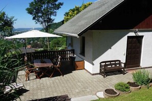 En terrasse med et bord, stole, en bænk og en hvid parasol.