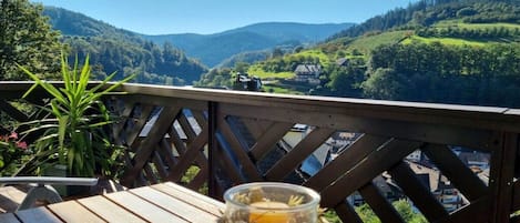 A wooden deck with a table and a glass jar with a candle, overlooking a valley with houses and greenery.