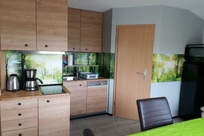 A compact kitchen with wooden cabinets, a dishwasher, and a coffee maker. - Holiday home on the Werra (Gerstungen\/OT Lauchröden)