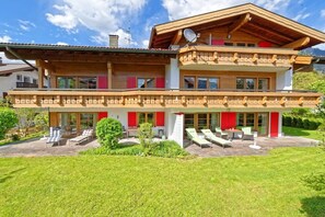 Eine zweistöckige Chalet mit Balkon, Sitzgelegenheit im Freien und einem gepflegten Rasen.