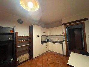 A compact kitchen with white cabinets, a microwave, and a wooden shelf unit. - Appartamento 80mq, due camere da letto (porto viro)