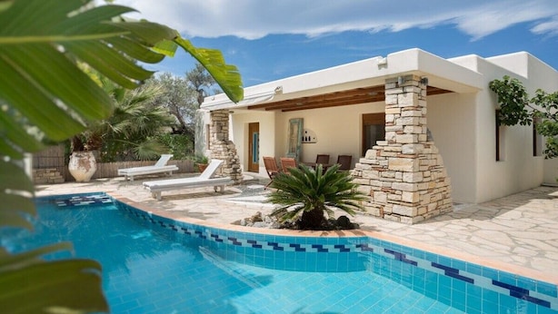 Et moderne hus med swimmingpool, stenstolper og en terrasse med liggestole.