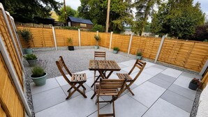 Un patio con mesa y sillas de madera, rodeado de una valla de madera y plantas en macetas.