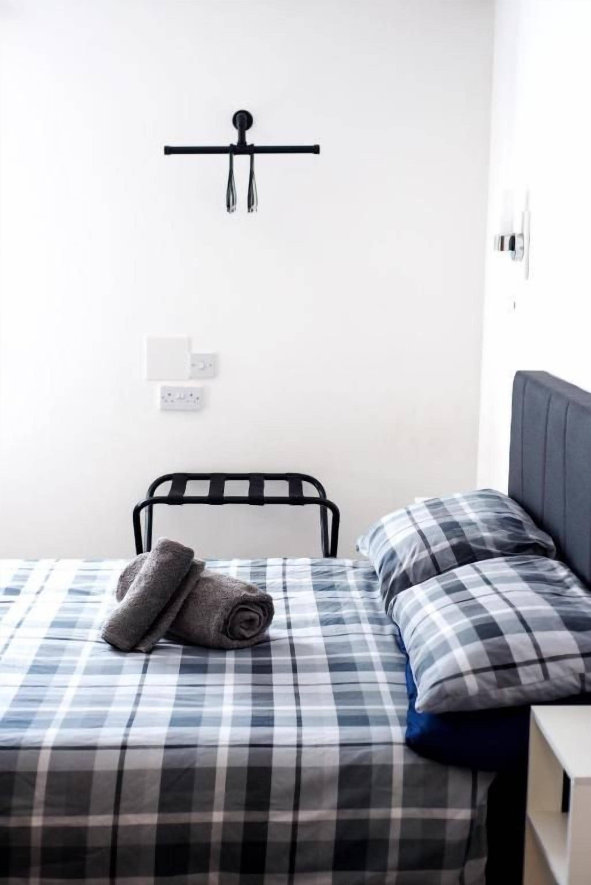A single bed with a checkered bedspread, a rolled towel, and a headboard.