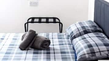 A single bed with a checkered bedspread, a rolled towel, and a headboard.