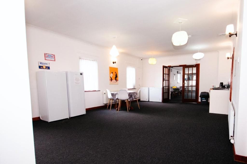 A room with a dining table and chairs, a refrigerator, and a kitchenette area.