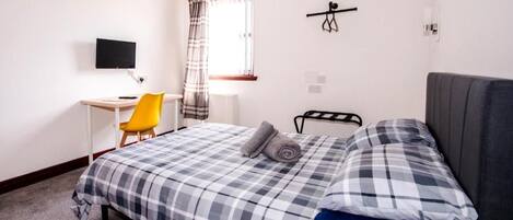 A bedroom with a bed, a desk, a chair, a television, and a window with curtains.