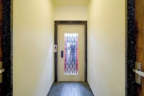 A hallway with a door at the end, a light switch on the wall, and a security camera above the door. - Collection O Satya Sai Square (Indore)