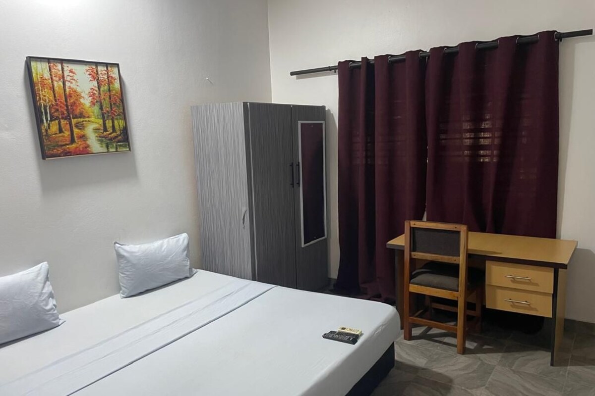 A bedroom with a bed, a desk, a chair, a wardrobe, and a painting on the wall.