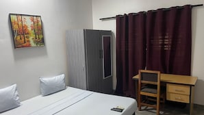 A bedroom with a bed, a desk, a chair, a wardrobe, and a painting on the wall.