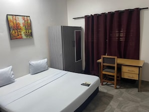 A bedroom with a bed, a desk, a chair, a wardrobe, and a painting on the wall.