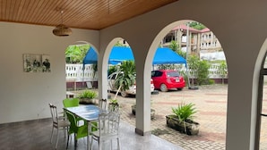 A covered patio with a dining table and chairs, a view of a red car, and potted plants.