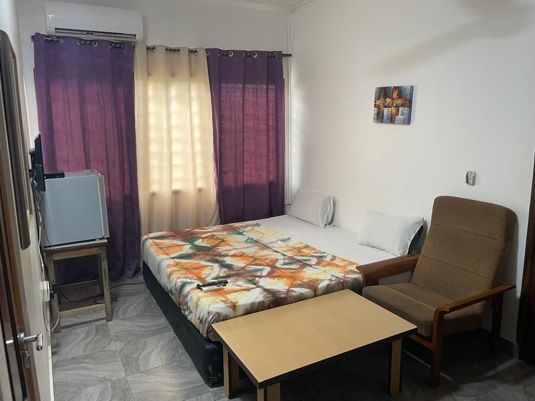 A hotel room with a bed, a chair, a small table, and curtains.