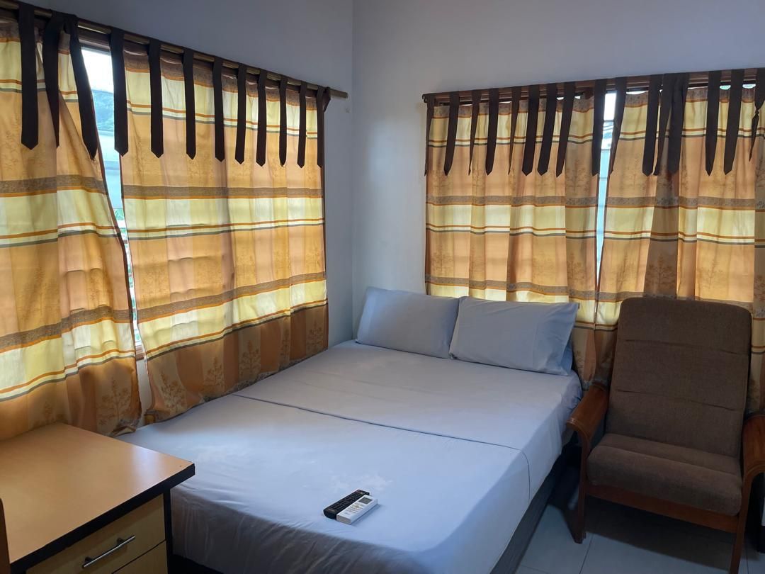 Un lit simple avec un matelas et des oreillers blancs, une table de chevet en bois avec un tiroir, une chaise marron et des rideaux à rayures.