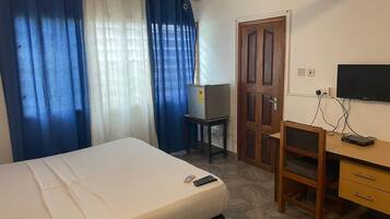 Quarto de hotel com cama, escrivaninha, cadeira, televisão e porta.