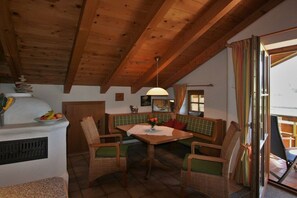 Uma área de refeições acolhedora com uma mesa e cadeiras de madeira, um banco e vista através de uma porta de vidro.