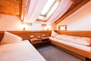 Um quarto aconchegante com claraboia, paredes de madeira, uma cama, uma mesinha de cabeceira com abajur e um pequeno quadro na parede.