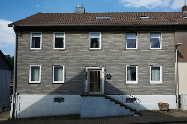 Un edificio de dos pisos con fachada de ladrillo gris, marcos de ventana blancos y techo de tejas marrones.