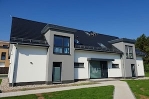 Ett modernt hus i två våningar med ett platt tak, stora fönster och en asfalterad uppfart.