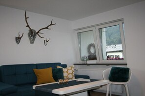 Un salon avec un canapé bleu, une table basse blanche et une fenêtre décorée d’une guirlande.