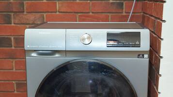 A front-loading Hisense washing machine with a control panel, set against a brick wall.