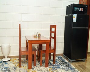 Un pequeño comedor con una mesa y sillas de madera, un refrigerador negro y un bote de basura blanco.