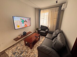 Una sala de estar con televisor de pantalla plana, un sofá de cuero, una mesa de centro de madera y un tapete estampado.