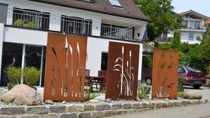 Een modern gebouw met een balkon, een metalen sculptuur en een geparkeerde auto.