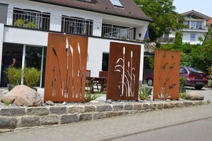 Un edificio moderno con un balcone, una scultura in metallo e un'auto parcheggiata.