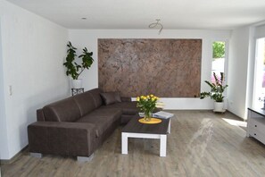 A modern living room with a sectional sofa, a coffee table with a vase of flowers, and a large abstract painting on the wall. - Sea area 85 square meters (Überlingen)