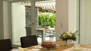 Un coin repas avec une table dressée pour deux personnes, un gâteau sur un présentoir en verre et une plante en pot.