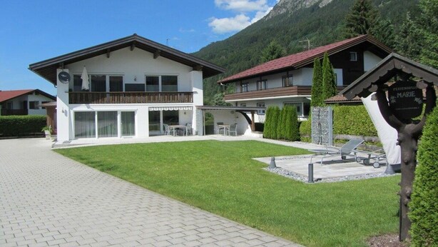 Un bâtiment moderne à deux étages, doté d’un balcon, d’une allée pavée et surplombant un paysage montagneux.