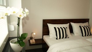 Une chambre d’hôtel avec un lit, des oreillers blancs, une table de chevet, une lampe de chevet et une orchidée en pot.