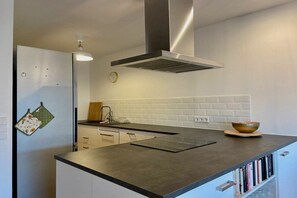 A modern kitchen with a central island, a stainless steel range hood, white subway tiles, and a small clock on the wall. - Holiday apartment with 1 bedroom (Sigmarszell)