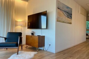 A modern living room with a flat-screen TV mounted on the wall, a dark blue chair, a wooden cabinet, and a white furry rug. - Holiday apartment with 1 bedroom (Sigmarszell)