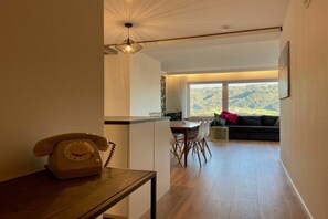 A modern interior with a wooden telephone, a dining area with chairs, a sofa, and a large window offering a view of a mountainous landscape. - Holiday apartment with 1 bedroom (Sigmarszell)
