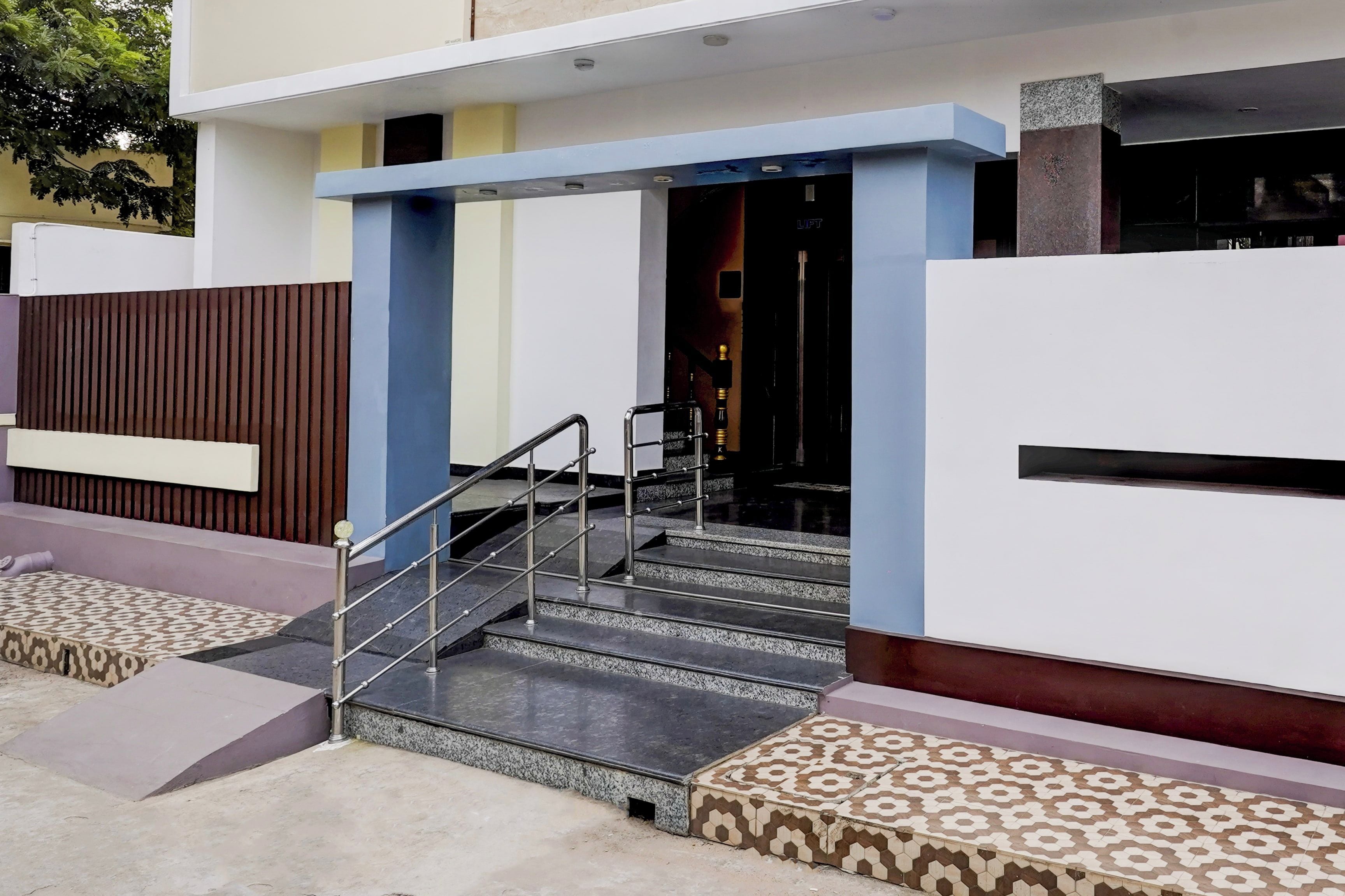 Entrada moderna de un edificio con una escalera que conduce a una puerta con la inscripción 'LUST'.