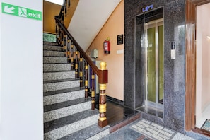 A staircase with a wooden handrail and a fire extinguisher mounted on the wall. - OYO Hotel O GT Road Nellore (Nellore)