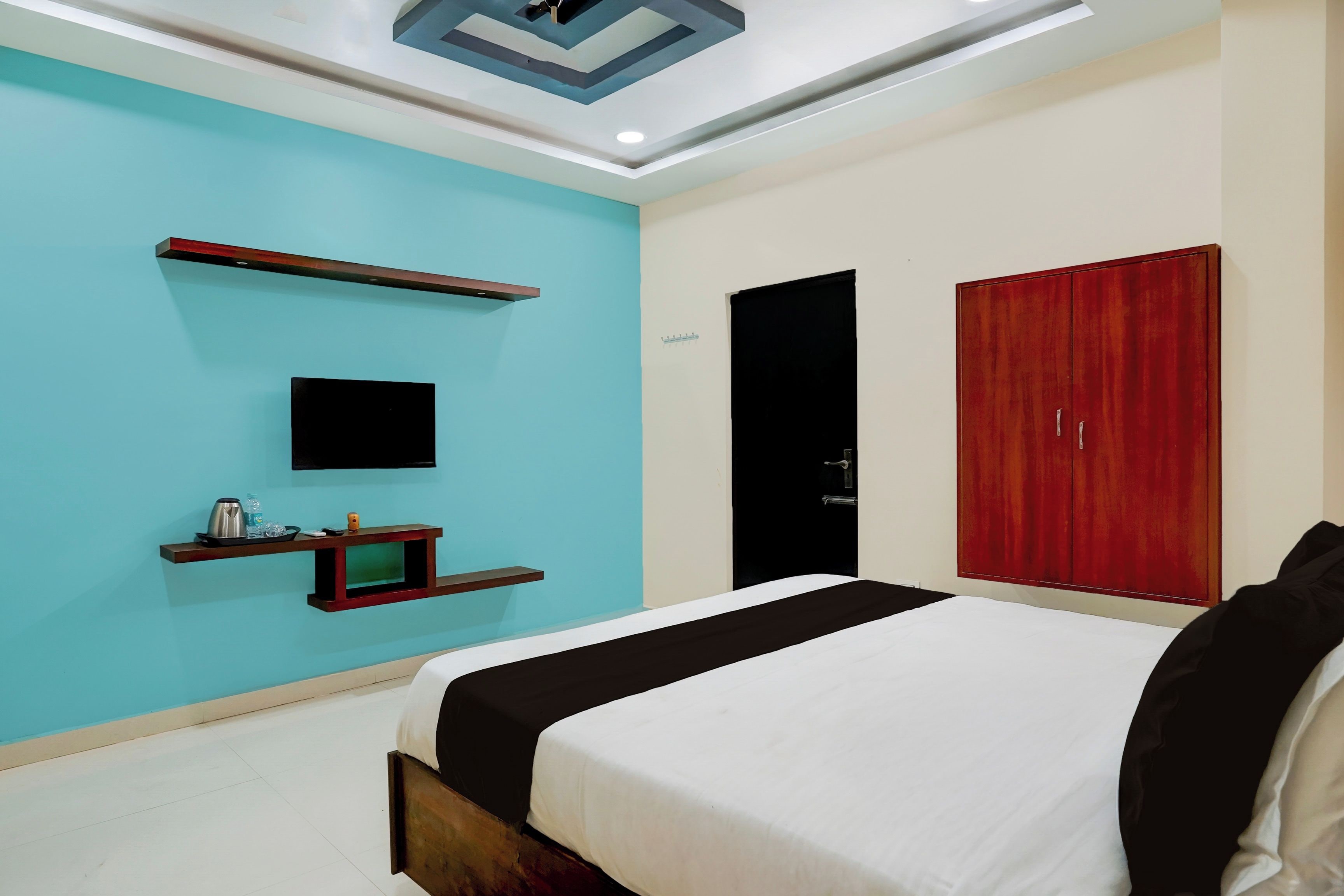 A bedroom with a bed, a TV, a wardrobe, and a shelf with items.
