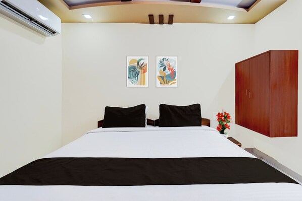 A hotel room with a bed, two wall-mounted artworks, a wooden wardrobe, and a small table with a vase of flowers. - OYO Hotel O GT Road Nellore (Nellore)