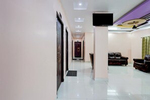 Un hall de hotel con mostrador de recepción, un televisor de pantalla plana en la pared, un área de descanso con sofás de cuero y un piso de baldosas.