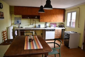 Eine kompakte Küche mit Holzausbau, einem Esstisch mit Stühlen, einer Kaffeemaschine und einem kleinen Backofen.