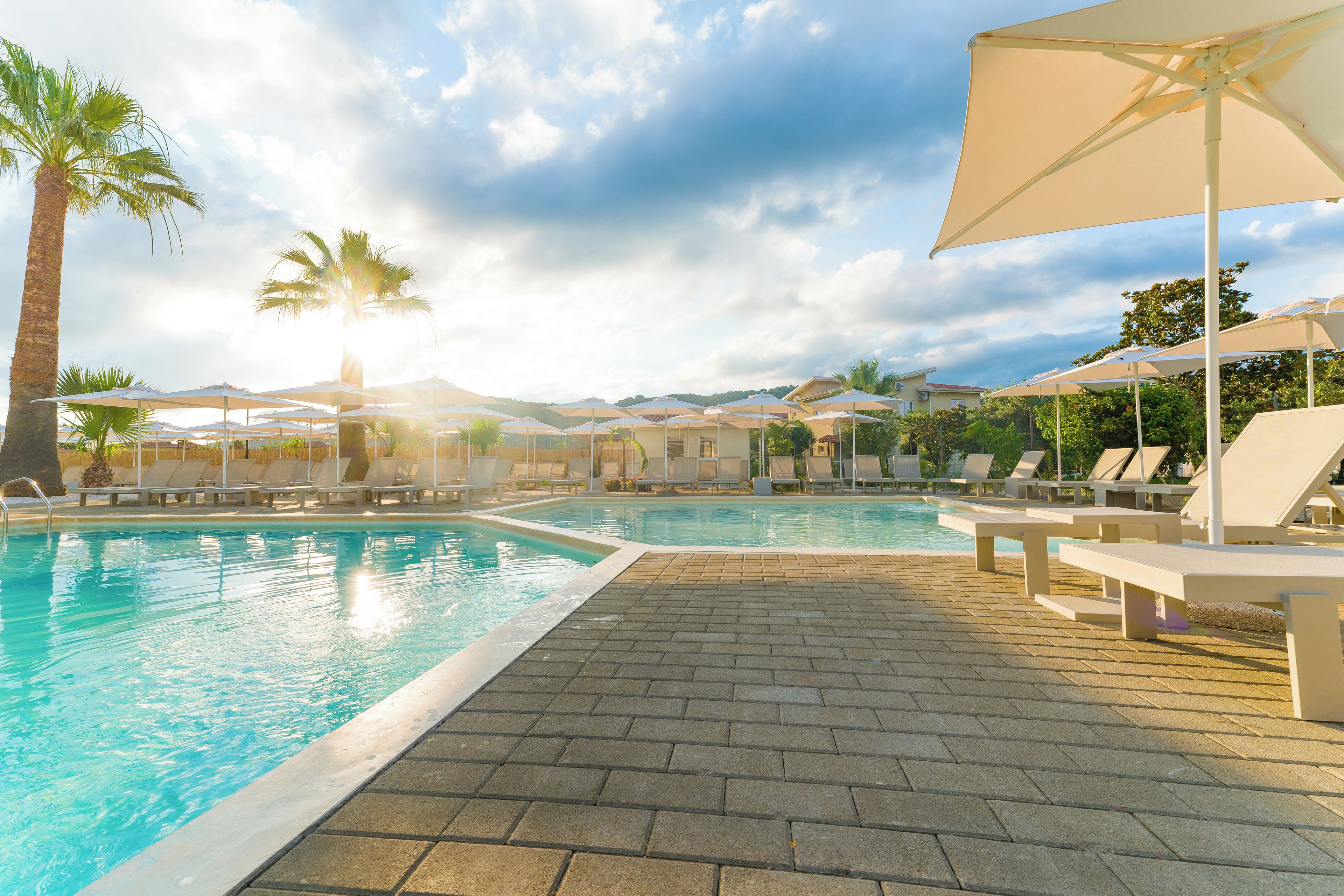 A swimming pool with lounge chairs and umbrellas, surrounded by palm trees and a clear sky.