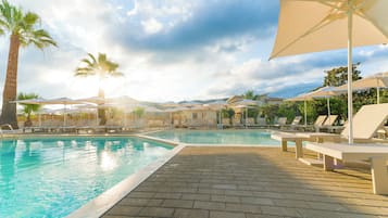 A swimming pool with lounge chairs and umbrellas, surrounded by palm trees and a clear sky.