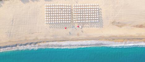 An aerial view of a beach with rows of white umbrellas and a few red chairs.