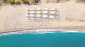 An aerial view of a beach with rows of white umbrellas and a few red chairs.