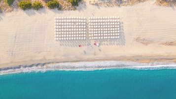 An aerial view of a beach with rows of white umbrellas and a few red chairs.