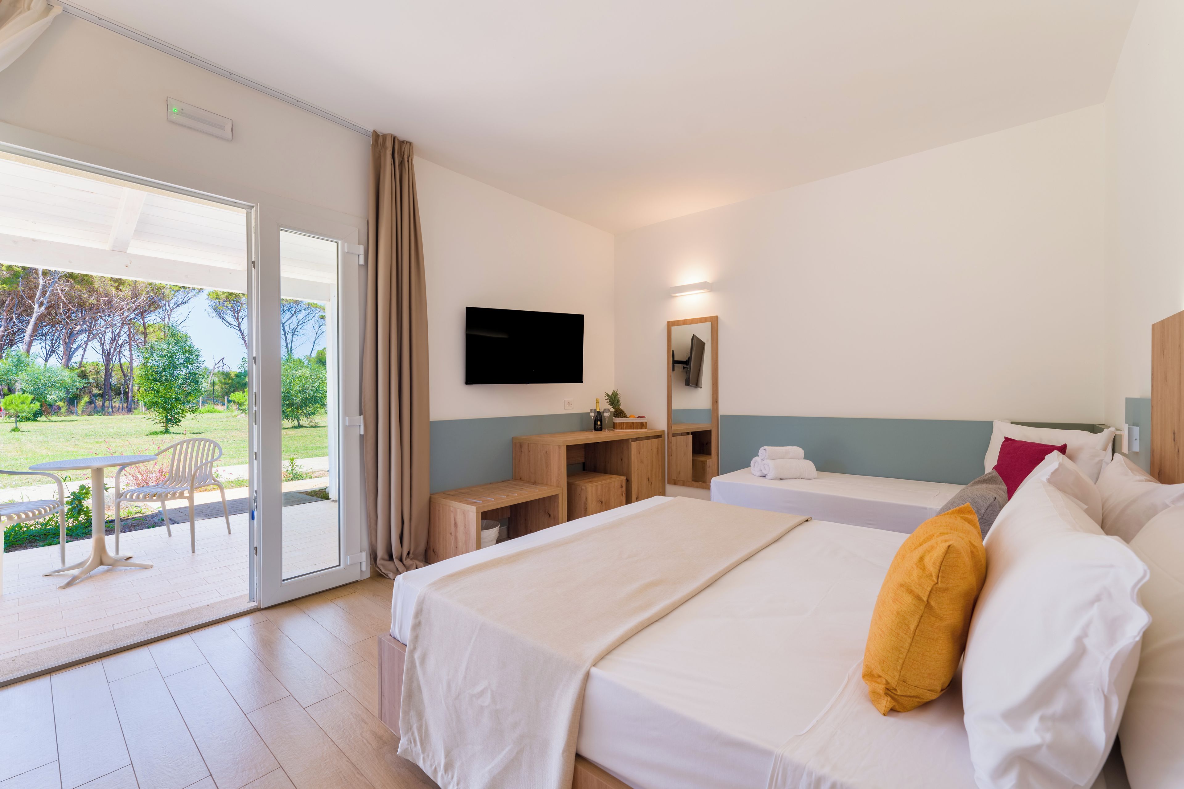 A hotel room with a bed, a desk, a TV, and a balcony with a table and chairs.