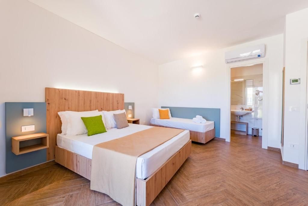 A hotel room with a large bed, bedside tables, a nightstand, a bathroom with a sink and mirror, and an air conditioning unit.