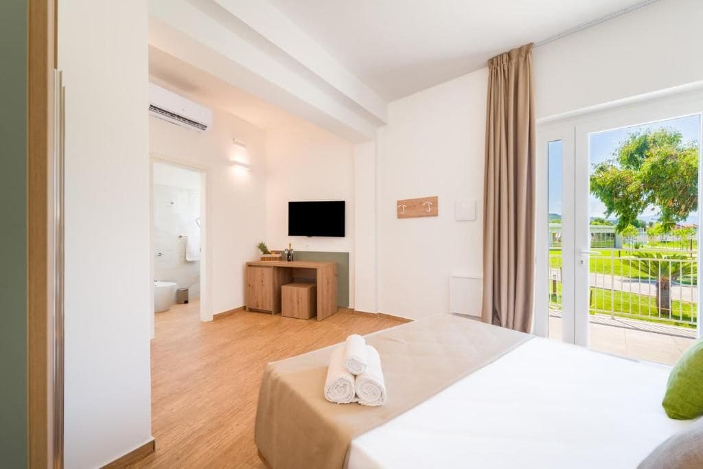 Camera d'albergo con un letto, una scrivania, una televisione e un balcone vista verde.